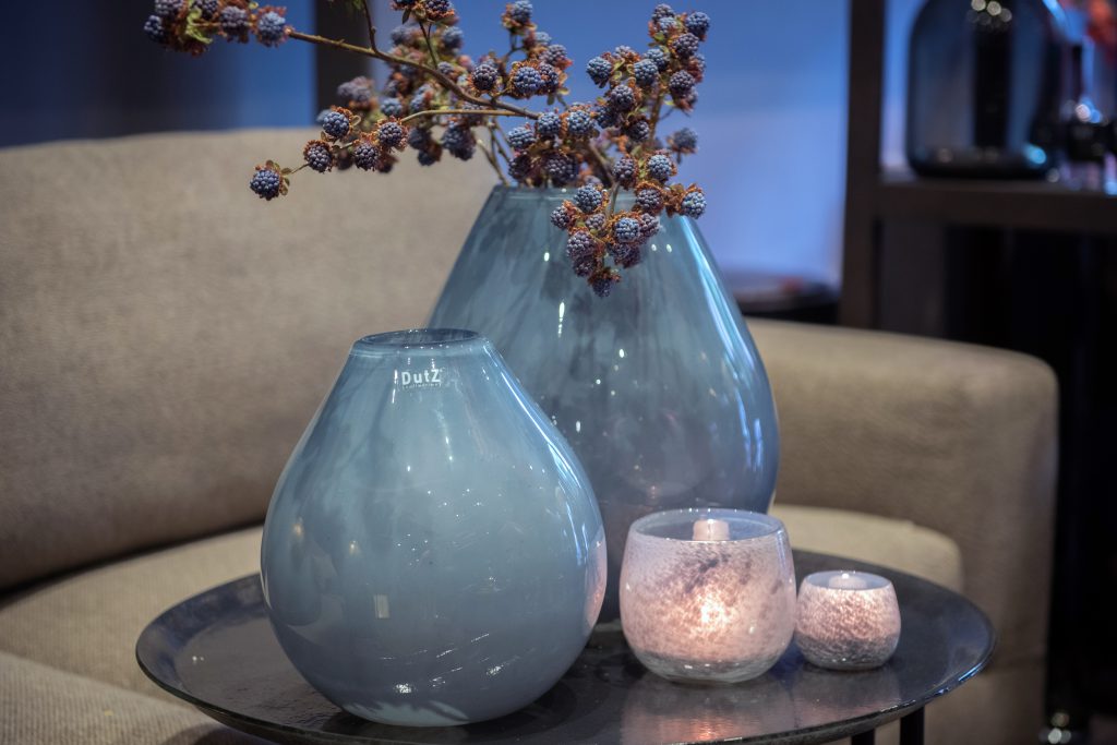 Druba vases and flowerpots in the colour jeans on a glass plate in a livingroom