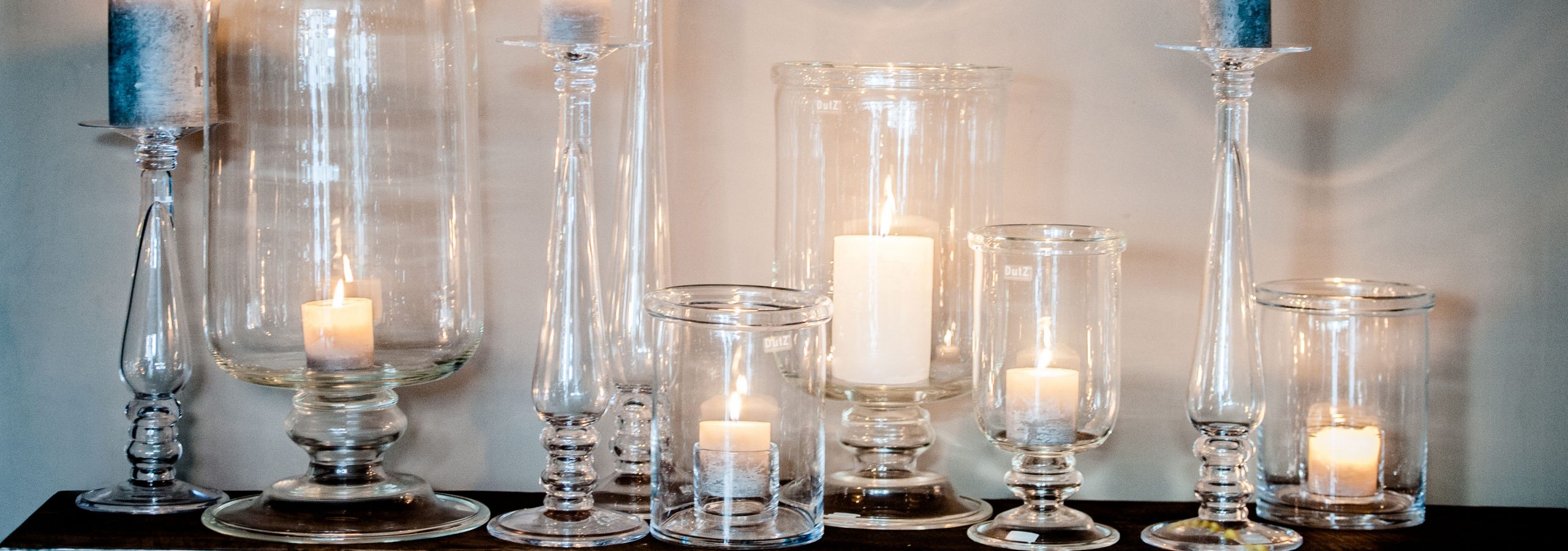 Glass candleholders and hurricanes with burning candles on a side-table